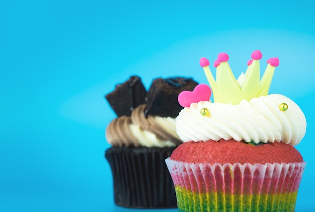 König Cupcake Rainbow Muffin mit Schokoladenschokoladenkuchenkleinen kuchen auf blauem Hintergrund