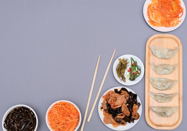Köstliche asiatische Knödel auf Holzplatte mit Stäbchen und verschiedenen Salaten auf grauem Hintergrund Selektiver Fokus Asiatisches Lebensmittelkonzept