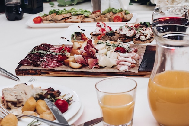 Köstliche Aufschnittplatte auf dem Tisch. Blick über die Hochzeitsfeier mit Aufschnittplatte, Obst- und Beerensaft und Teller mit Hauptgericht.