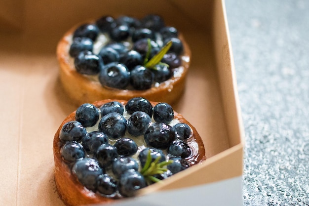 Köstliche Blaubeer-Törtchen mit Vanillepuddingcreme in einem Karton auf grauem Hintergrund