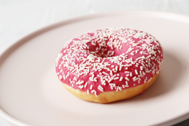 Köstliche bunte Donuts mit Streuseln auf stilvollem Teller auf weißem Tisch mit Konfetti, flach. Party-Konzept. Keine Diät. Schokoriegel bei der Hochzeitsfeier. Lila und rosa Donuts