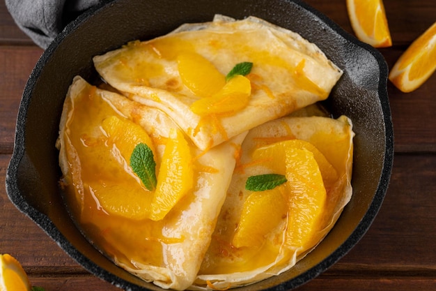 Köstliche Crêpes-Suzette mit Orangensirup und geschnittenen Früchten auf einer Bratpfanne