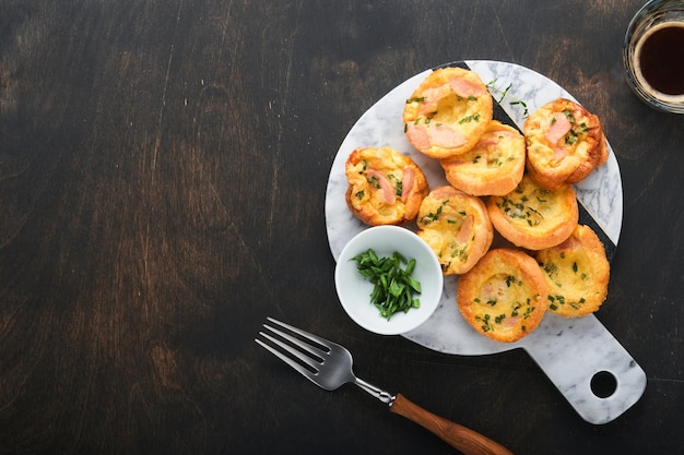 Köstliche Ei-Muffins mit Frühlingszwiebeln, Speck, Käse und Tomaten auf Holzbrett auf altem rustikalem Holzhintergrund Gesundes proteinreiches und kohlenhydratarmes Frühstück Hausgemachte Speisen