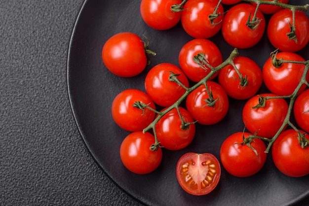 Köstliche frische Kirschtomaten auf den Zweigen als Zutat zum Kochen eines vegetarischen Gerichts auf dunklem Betongrund