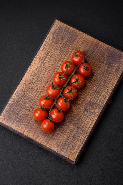 Köstliche frische Kirschtomaten auf einem Zweig auf dunklem Betonhintergrund