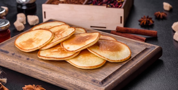 Köstliche frische Pfannkuchen auf einem Holzschneidebrett mit Zucker auf dunklem Betongrund