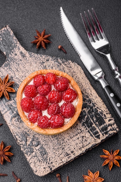 Köstliche, frische, süße, runde Torte mit reifen Himbeeren und Sahne auf dunklem Betongrund