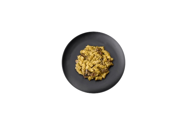 Köstliche Fusilli-Nudeln mit grüner Pesto-Sauce mit Salz und Gewürzen auf einem Keramikteller auf dunklem Betongrund