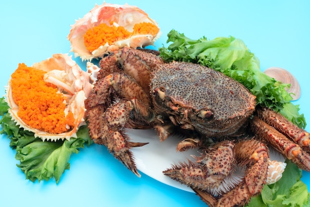 Köstliche gedämpfte Krabbe liegt auf einem weißen Teller auf blauem Hintergrund mit Orangenkrabbenkaviar und grünem Salat