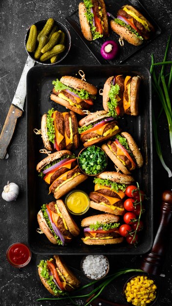 Köstliche gegrillte hausgemachte Burger mit Rindfleisch, Tomaten, Käse, Zwiebeln und Salat. Burger-Menü. Ansicht von oben. Auf einem schwarzen Steinhintergrund.