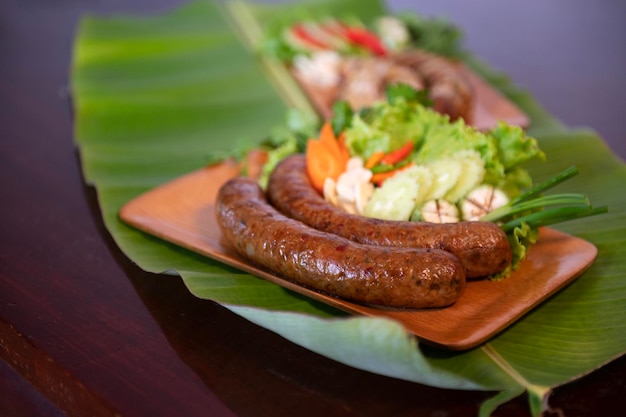 Köstliche gegrillte Schweinswurst mit Kräutern vom Grill, serviert im Restaurant Nahaufnahme von thailändischer Wurst mit Beilage aus frischem Gemüse Thailändisches Essen