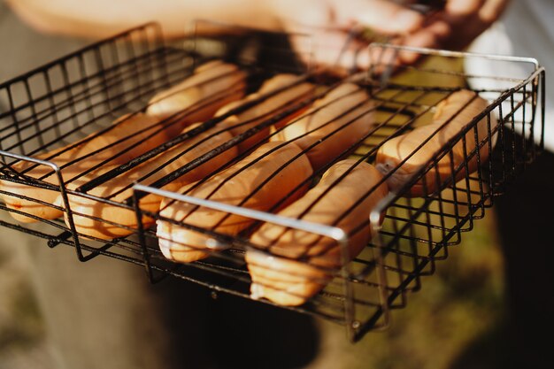 Köstliche gegrillte Würstchen, die auf dem Eisengitter eines tragbaren Grills über glühenden Kohlen ruhen, während sie perfekt kochen