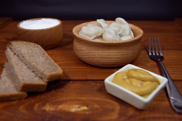 Köstliche gekochte Knödel auf einem hölzernen Hintergrund mit Senfsauce, Sauerrahm und Brot