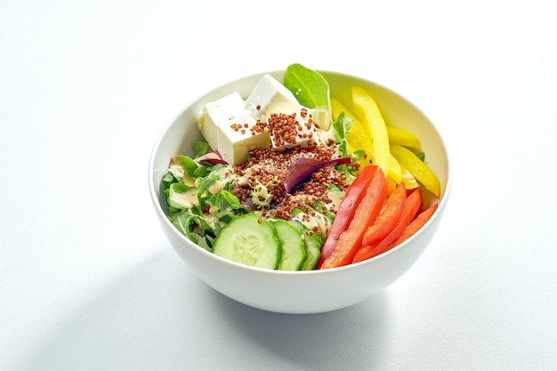 Köstliche Gemüseschüssel mit Gurke, Paprika, Salatmischung, Quinoa und Tofu in einem weißen Teller. Auf grauer Oberfläche isoliert.