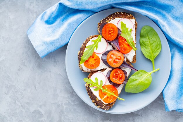 Köstliche geröstete Sandwiches mit Frischkäse, Kirschtomaten und Rettich auf grauem Teller