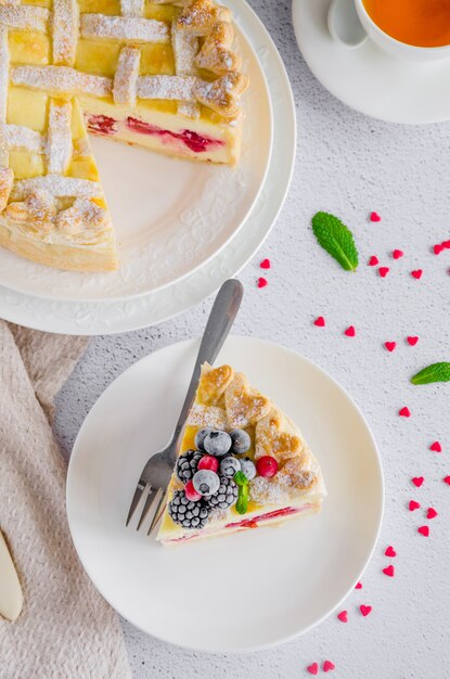 Köstliche hausgemachte Blätterteigpastete oder Kuchen mit Frischkäsefüllung und Kirsche auf einem weißen Teller auf einem hellen Steinhintergrund.