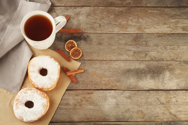 Köstliche hausgemachte Donuts mit Zuckerpulver und eine Tasse Tee auf einem Holztisch