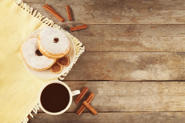Köstliche hausgemachte Donuts mit Zuckerpulver und Tasse Kaffee auf Holztisch