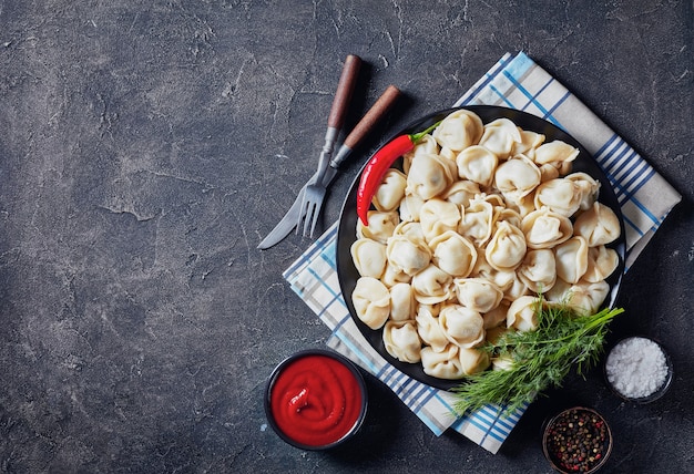 Köstliche heiße Knödel serviert auf einem schwarzen Teller mit Dill und Tomatensauce, Ansicht von oben, Flatlay, Kopierraum