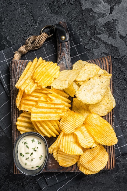 Köstliche Kartoffelchips Crinkle hausgemachtes heißes BBQ auf einem Holzbrett Schwarzer Hintergrund Draufsicht