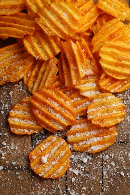 Köstliche Kartoffelchips mit Salz auf Holztisch Nahaufnahme