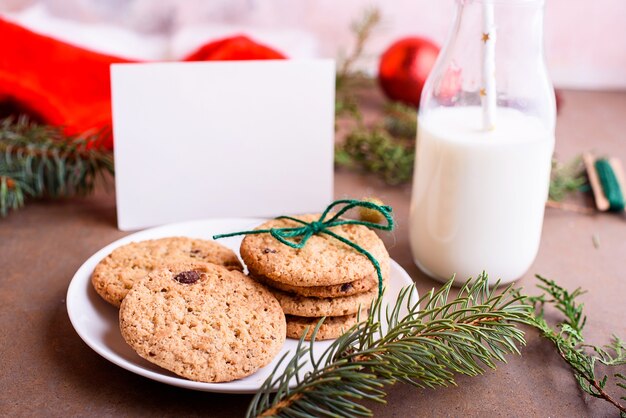 Köstliche kekse mit schokolade auf einem weißen teller, milch, weihnachtsmütze, verspotten für text. brief und kekse für den weihnachtsmann.