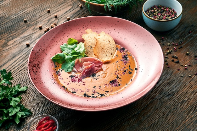 Köstliche Kokosnuss- und Linsencremesuppe mit Croutons und Jamon in einem roten Teller auf einem Holztisch. Restaurant Essen. Nahaufnahme