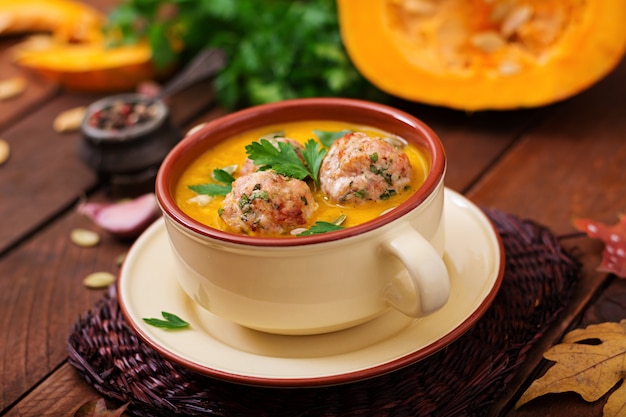 Köstliche Kürbiscremesuppe mit Fleischbällchen aus Putenhackfleisch in einer Schüssel auf einem Holztisch.