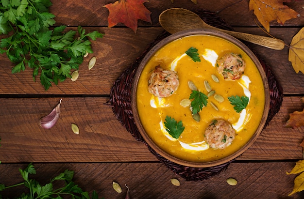 Köstliche Kürbiscremesuppe mit Fleischbällchen aus Putenhackfleisch in einer Schüssel auf einem Holztisch.