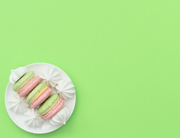 Köstliche Macarons mit weißen Merengues auf weißer Platte auf grünem Hintergrund