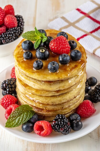 Köstliche Pfannkuchen mit frischen Beeren auf weißem Holztisch