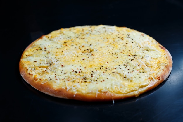 Köstliche Pizza mit vier Käsesorten mit Cheddar, Parmesan, Mozzarella und Tomatensauce auf schwarzem Hintergrund. Sicht von oben.