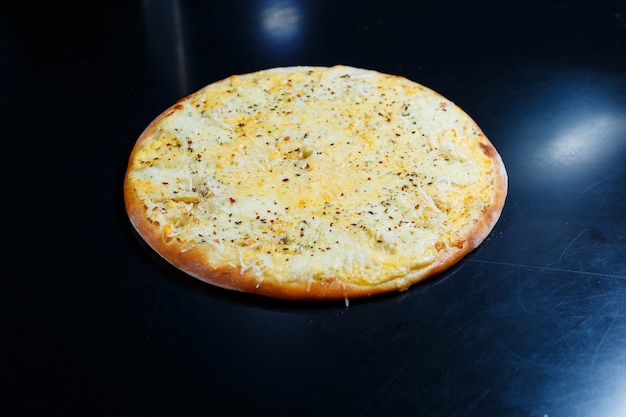 Köstliche Pizza mit vier Käsesorten mit Cheddar, Parmesan, Mozzarella und Tomatensauce auf schwarzem Hintergrund. Sicht von oben.