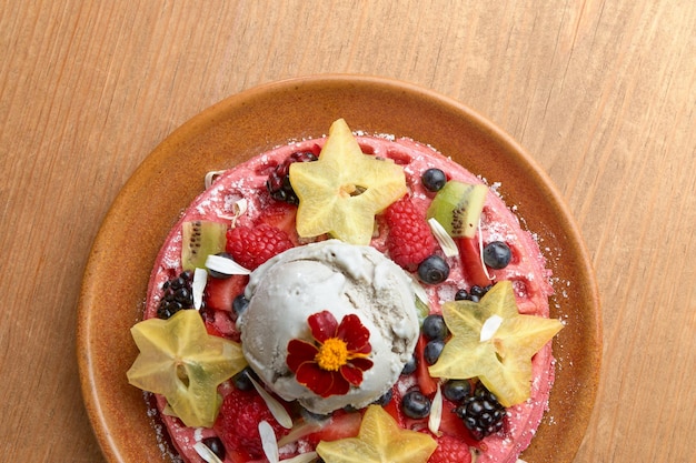 Köstliche rosa Eiswaffel mit roten Früchten und Sternfrüchten auf Holztisch