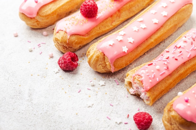 Köstliche rosa glasierte Eclairs mit Sahne-, Himbeer- und Zuckerstreuseln auf grauem Hintergrund, Kopierraum.