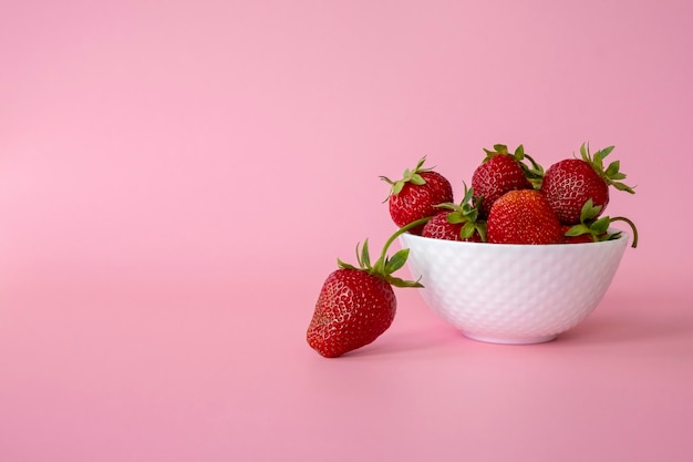 Köstliche saftige Erdbeeren in weißer Schüssel auf rosa Hintergrund. Gesunde Ernährung, Rohkost und Detox-Food-Konzept. Erdbeerernte auf dem Bauernhof. Platz kopieren.