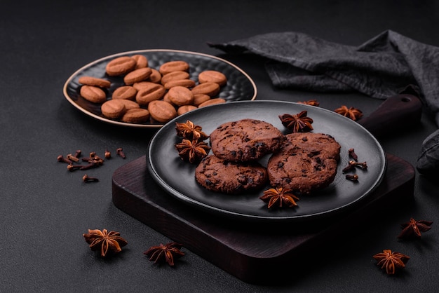 Köstliche Schokoladenkekse mit Nüssen auf einer schwarzen Keramikplatte auf dunklem Betonhintergrund