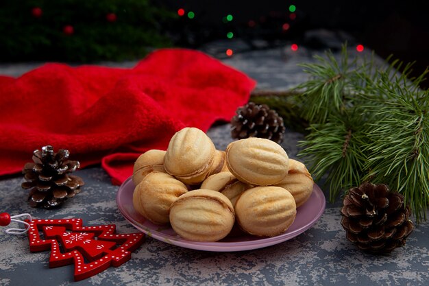 Köstliche Shortbread-Kekse in Form von Walnüssen mit einer Füllung aus süßer Kondensmilch und zerdrückten Nüssen auf dem Hintergrund eines Weihnachtsbaumes und von Lichtern. Weihnachtsgenuss.