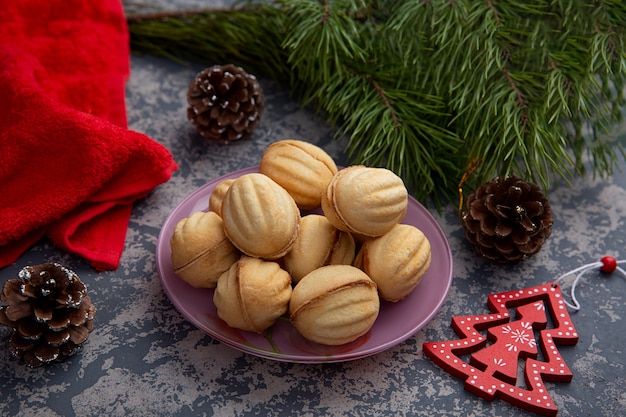 Köstliche Shortbread-Kekse in Form von Walnüssen mit einer Füllung aus süßer Kondensmilch und zerdrückten Nüssen auf dem Hintergrund eines Weihnachtsbaumes und von Lichtern. Weihnachtsgenuss.