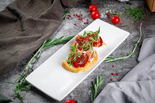 Köstliche Snacks Bruschetta mit Speck, gerösteten Tomaten, roten Zwiebelringen und Rucola. Geröstete Croutons mit getrocknetem Fleisch und Salat