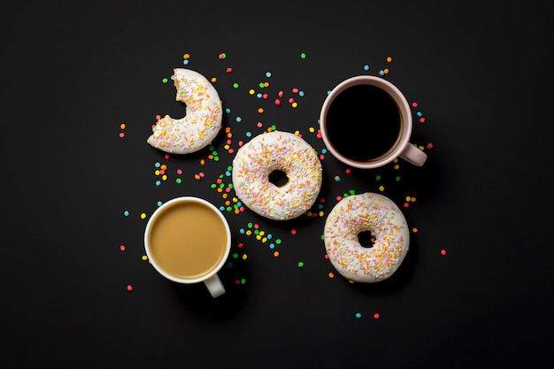 Köstliche, süße, frische Donuts, mehrfarbige dekorative Süßigkeiten, eine Tasse Kaffee auf schwarzem Hintergrund. Konzept von Frühstück, Fast Food, Café, Bäckerei. Flache Lage, Draufsicht.