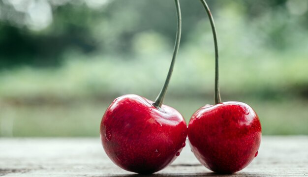 Köstliche süße Kirsche Nahaufnahme auf dem Holztisch mit sommergrünem Bokeh-Hintergrund, Sommerfrüchte mit hohem Vitamin- und Antioxidantiengehalt