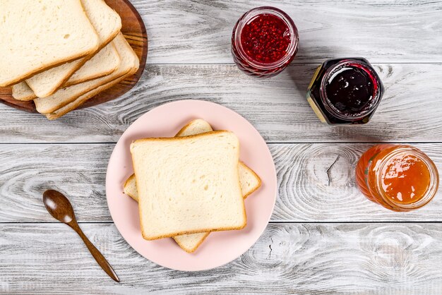 Köstliche Toasts auf rosa Teller mit süßen Marmeladen und bewaldetem Löffel auf Holztisch.