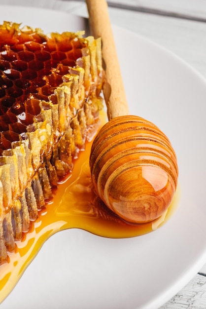 Köstliche Wabe auf weißer Platte mit Holzhonigschöpflöffel