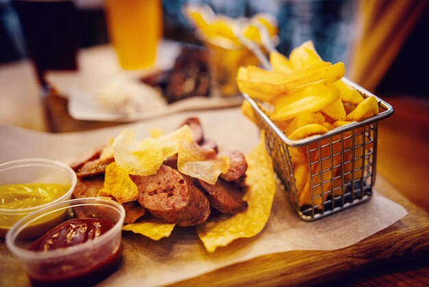 Köstliche Wurst mit Pommes Frites und Soße auf Holzbrett in Light Street Fast Food festivel Konzept gebratenes Fleischsteak und kaltes Bier trinkt stilvolles Servieren getönt