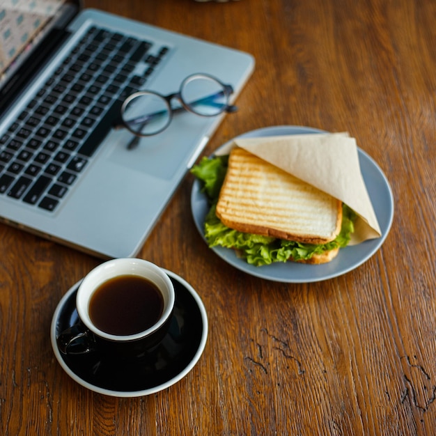 Köstlicher Americano-Kaffee auf Holztisch mit appetitlichem Sandwich und Laptop