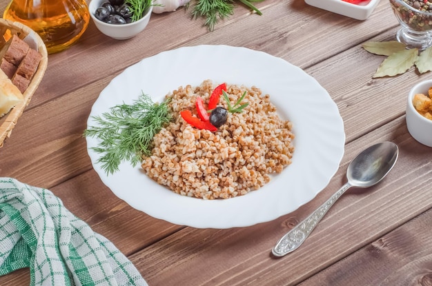 Köstlicher appetitanregender Buchweizenbrei, der in einem weißen Teller auf einem Holztisch garniert wird