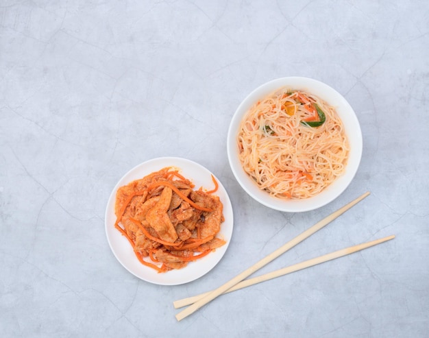 Köstlicher asiatischer Funchose-Salat und veganer Soja-Fleischsalat in weißen Schalen mit Holzstäbchen auf grauem Hintergrund Selektiver Fokus Asiatisches Lebensmittelkonzept