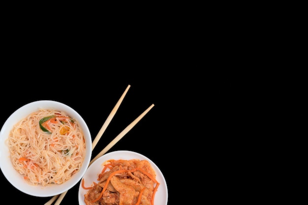Köstlicher asiatischer Funchose-Salat und veganer Soja-Fleischsalat in weißen Schalen mit Holzstäbchen auf schwarzem Hintergrund Selektiver Fokus Asiatisches Lebensmittelkonzept