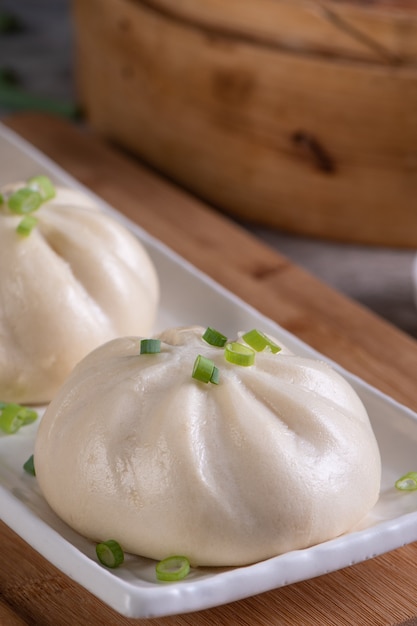 Köstlicher Baozi, chinesisches gedämpftes Fleischbrötchen ist fertig zum Essen auf Servierplatte und Dampfgarer, Nahaufnahme, Produktdesignkonzept für Kopienraum.